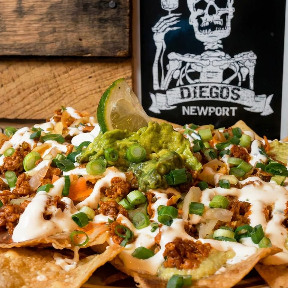 Loaded nachos topped with seasoned meat, guacamole, sour cream, melted cheese, vegetables, and lime, beside a Diegos Newport sign.